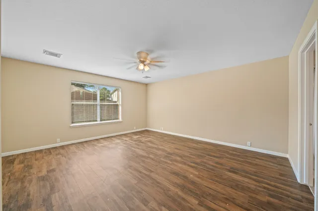 a view of an empty room with wooden floor and a window