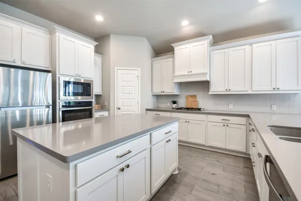 a kitchen with stainless steel appliances granite countertop a refrigerator a sink dishwasher a oven and white cabinets with wooden floor