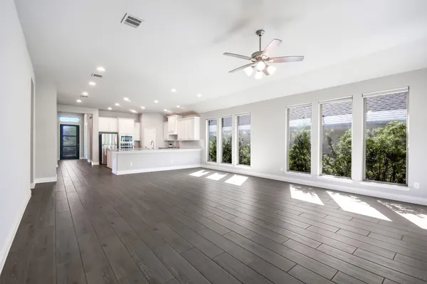a view of an empty room with wooden floor and a kitchen