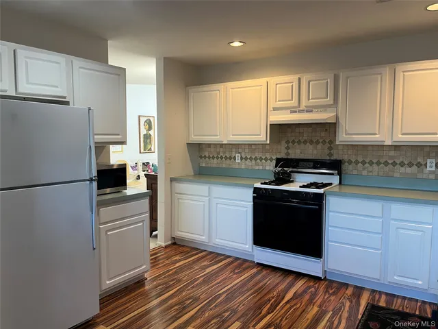 a kitchen with granite countertop a refrigerator stove and white cabinets