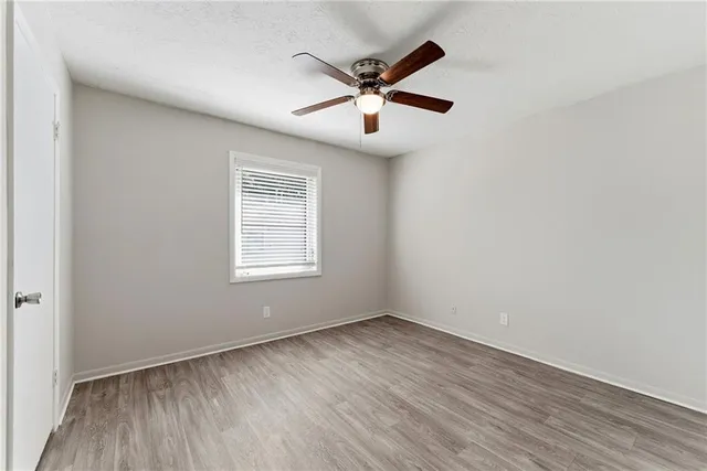 an empty room with wooden floor fan and windows