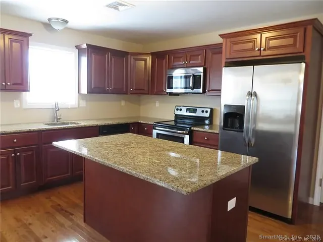 a kitchen with stainless steel appliances granite countertop a sink a microwave a refrigerator and wooden cabinets