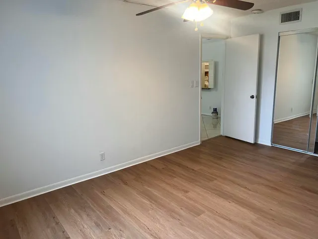 a view of an empty room with wooden floor and a chandelier fan