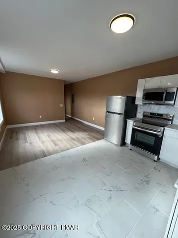 a view of kitchen and empty room with wooden floor