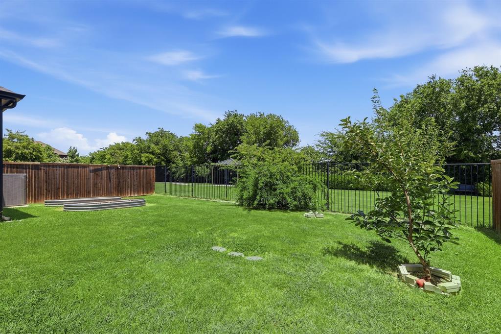 539 Farrell Lane Allen, TX 75013 - Photo 36 of 39 Expansive green lawn featuring a wood privacy fence, black metal fencing, mature trees, and a raised garden bed