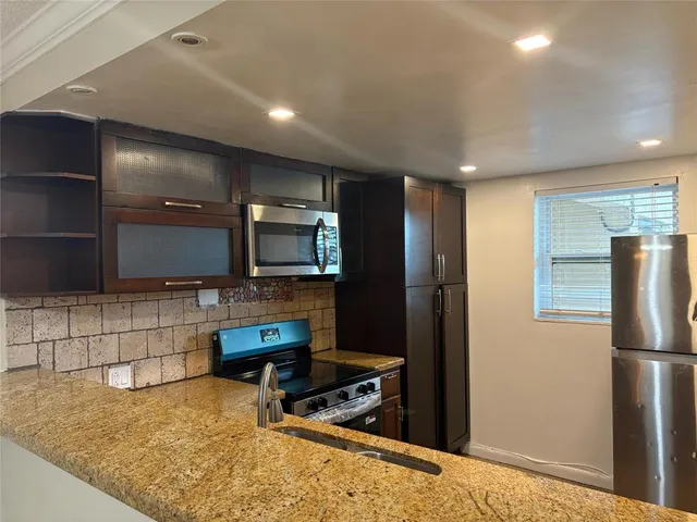 a kitchen with stainless steel appliances kitchen island granite countertop a refrigerator and a stove top oven