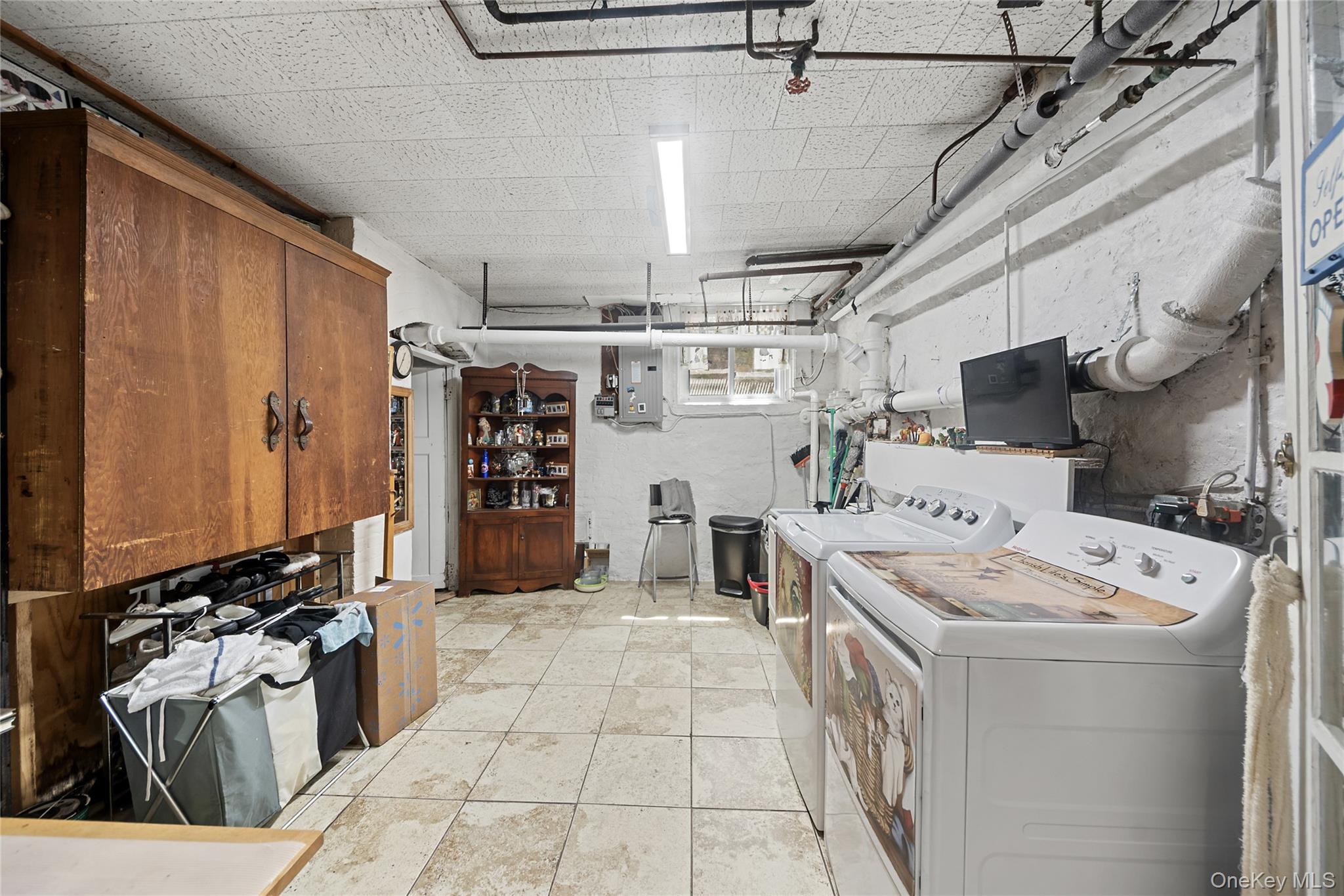 75 Chappaqua Road Briarcliff Manor, NY 10510 - Photo 30 of 50 Utility space featuring tiled flooring, exposed ceiling pipes, white painted brick walls, two laundry appliances, and built-in wood cabinetry