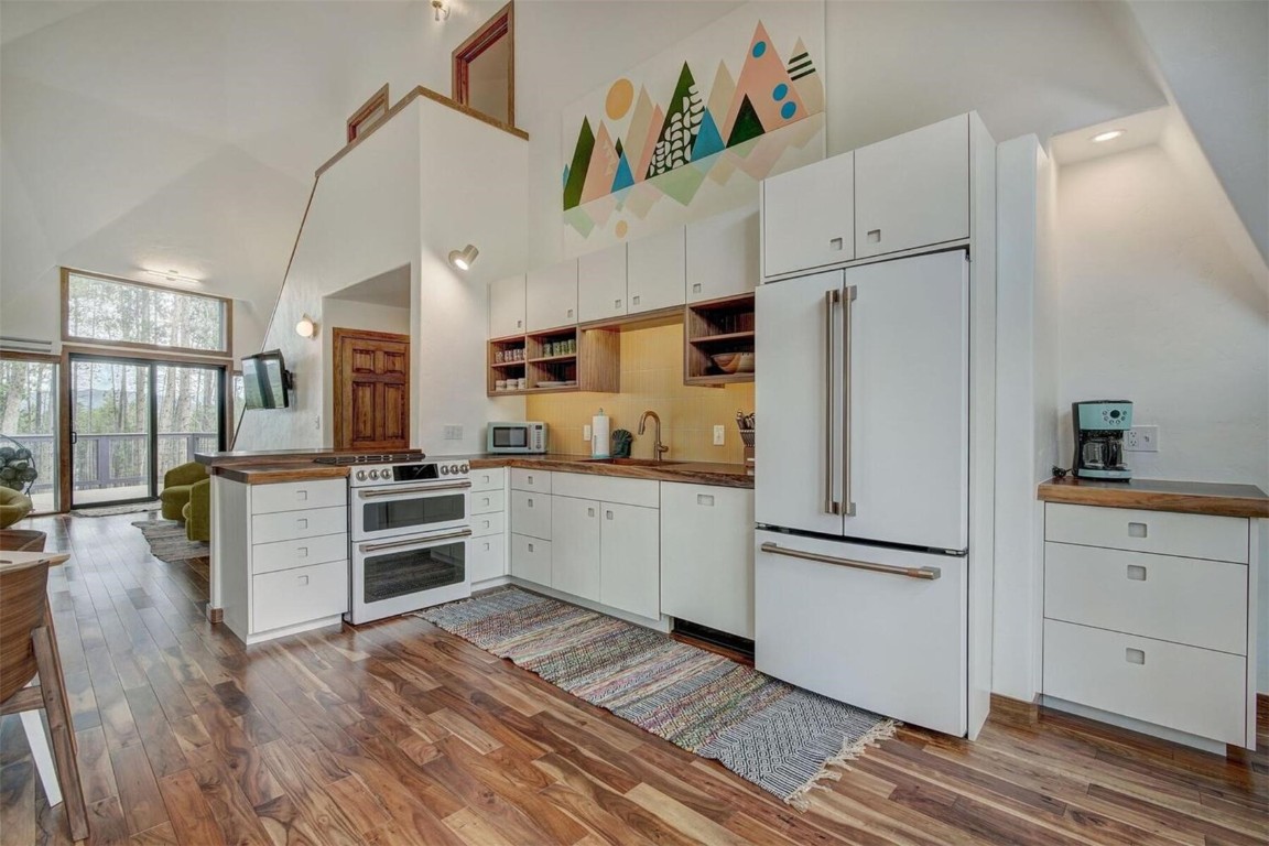 Kitchen featuring white appliances, white cabinetry, high vaulted ceiling, hardwood   flooring