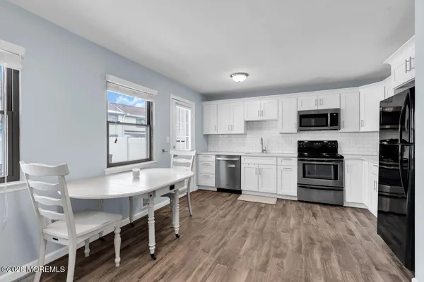 a large kitchen with stainless steel appliances a stove a sink dishwasher a microwave oven and a dining table with wooden floor