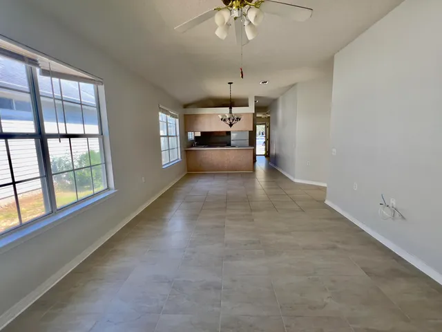 an empty room with chandelier fan and windows