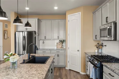 a kitchen with stainless steel appliances kitchen island granite countertop a refrigerator a sink dishwasher a stove and white cabinets with wooden floor