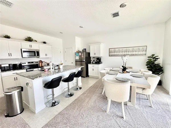 a living room with stainless steel appliances furniture a rug and a kitchen view