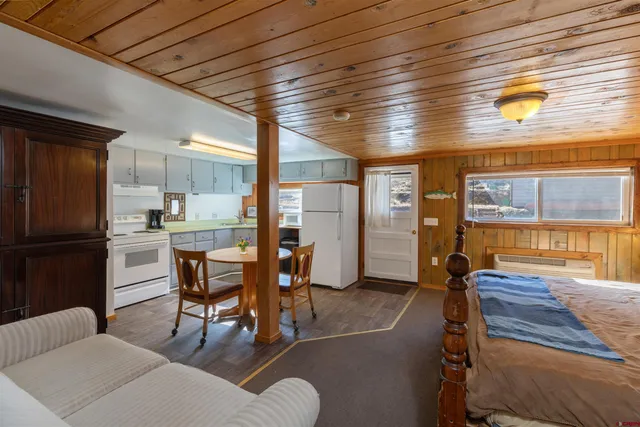 a living room with couches a dining table chairs and a refrigerator