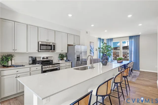 a kitchen with stainless steel appliances kitchen island granite countertop a stove a sink a refrigerator with white cabinets and wooden floor