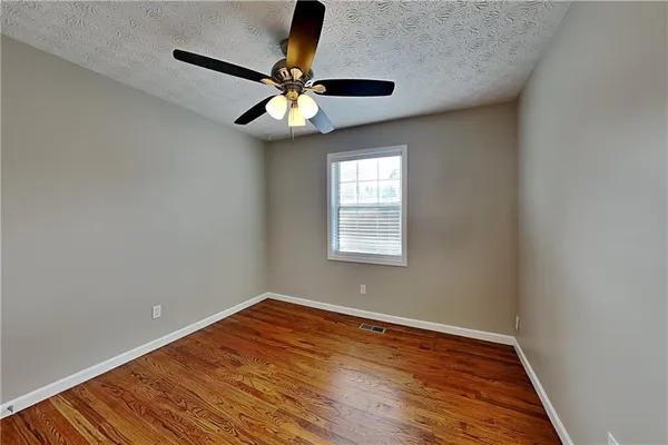an empty room with wooden floor fan and windows