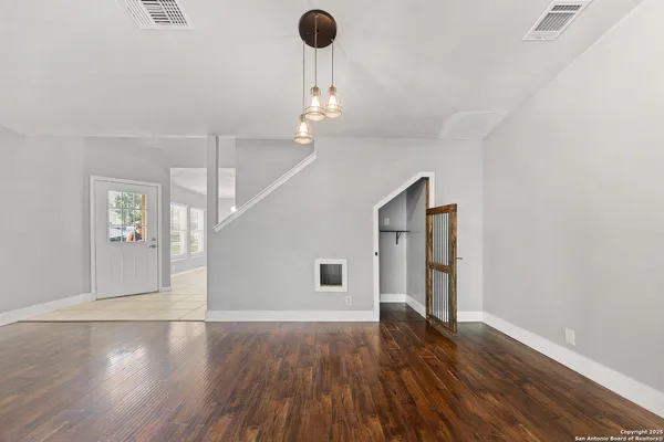 an empty room with wooden floor chandelier and windows