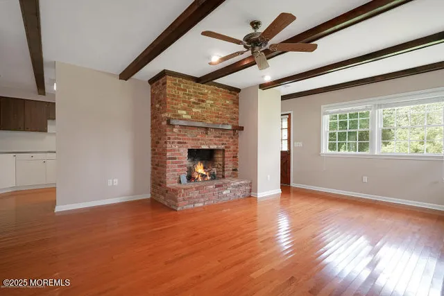 a view of an empty room with wooden floor fireplace and a window