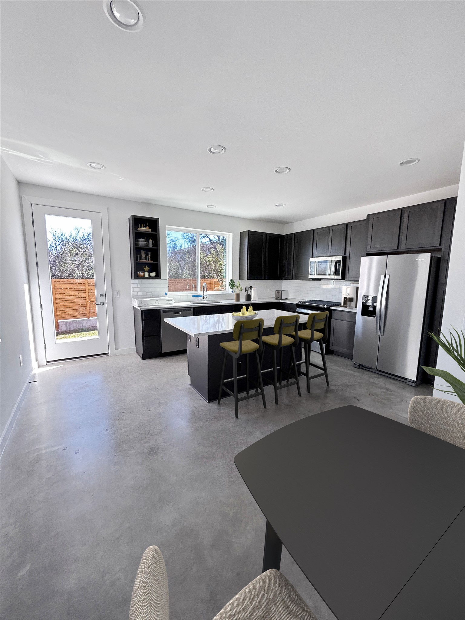 1191 Sarabeth Way Austin, TX 78721 - Photo 3 of 13 Kitchen with a breakfast bar area, appliances with stainless steel finishes, a kitchen island, finished concrete floors, and dark cabinetry