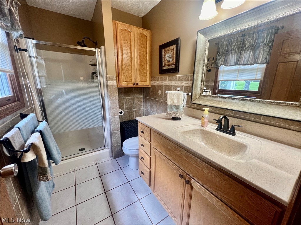 53360 High Ridge Road Bridgeport, OH 43912 - Photo 14 of 41 Bathroom featuring backsplash, toilet, a shower with shower door, vanity, and a textured ceiling
