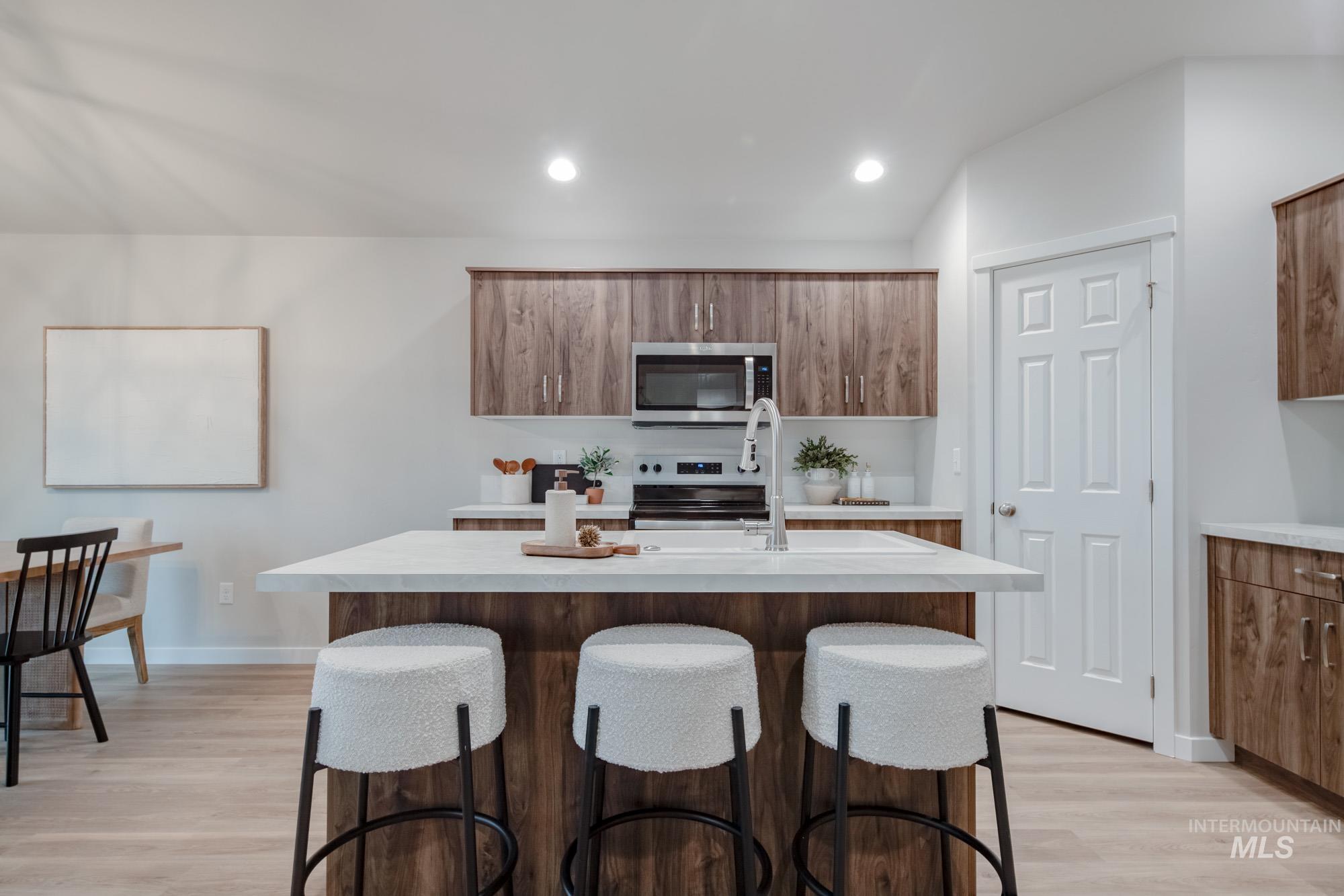1760 West Unforgettable Street Meridian, ID 83642 - Photo 10 of 26 Kitchen featuring an island with sink, brown cabinetry, a kitchen bar, recessed lighting, and light wood-style flooring