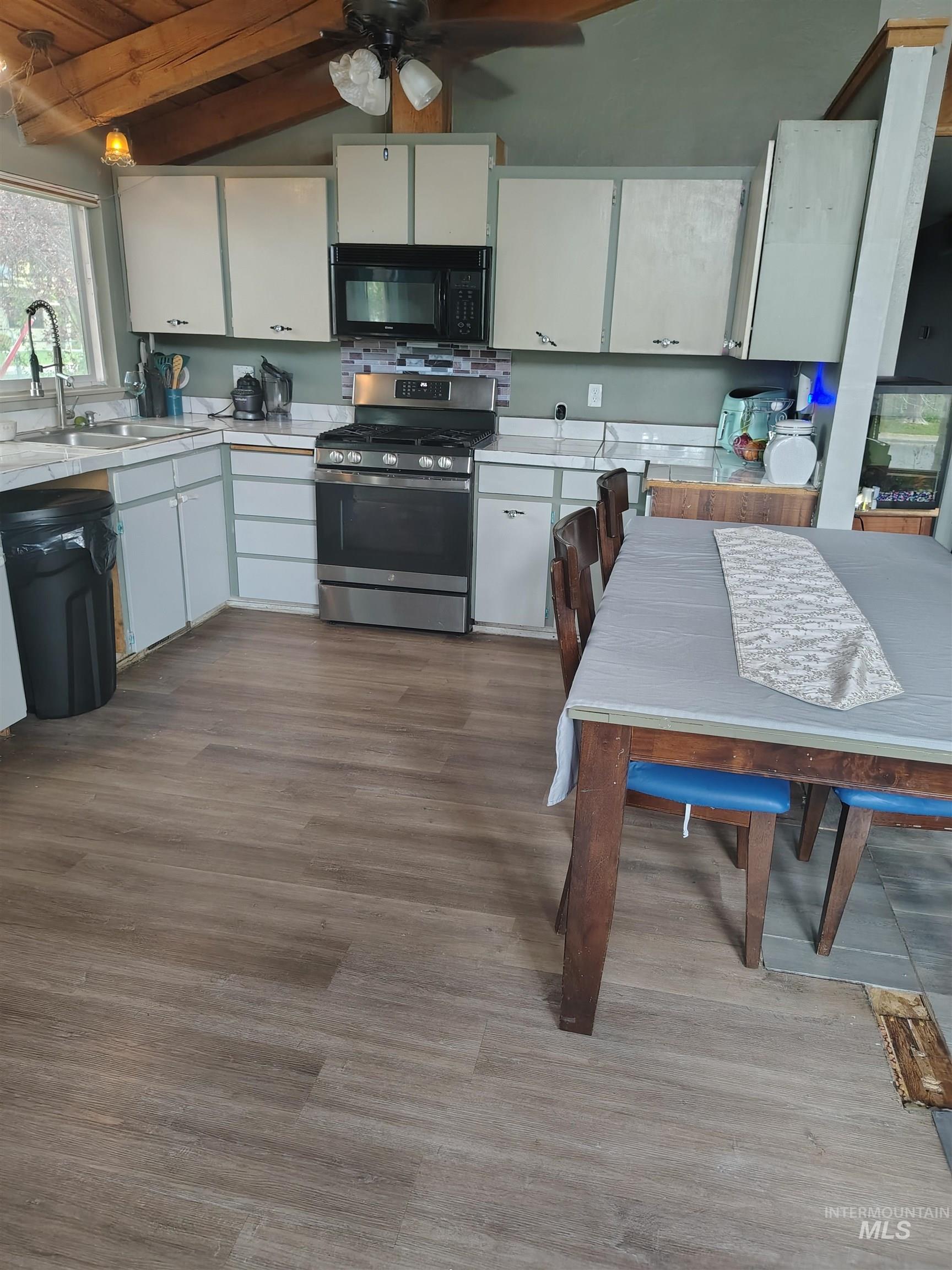 820 Meadows Drive Twin Falls, ID 83301 - Photo 11 of 23 Kitchen with white cabinets, stainless steel range with gas stovetop, light countertops, black microwave, and vaulted ceiling with beams