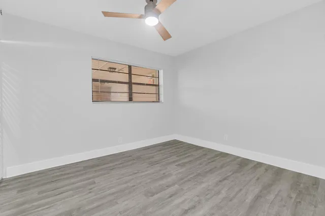 an empty room with wooden floor chandelier fan and windows