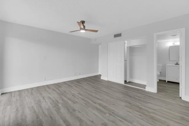 a view of an empty room with wooden floor and a ceiling fan