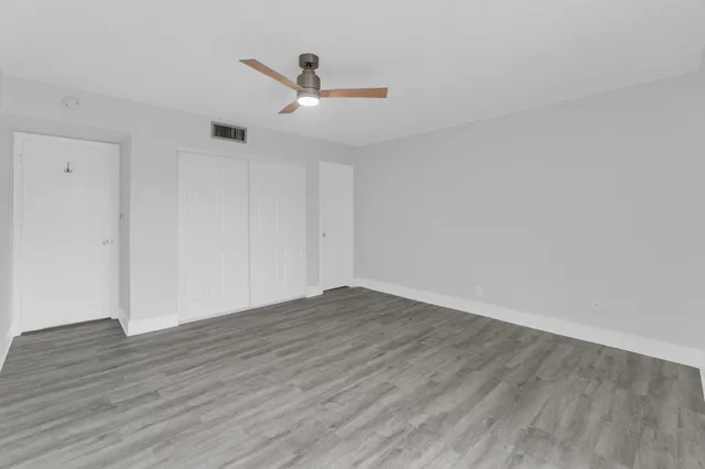 an empty room with wooden floor ceiling fan and window
