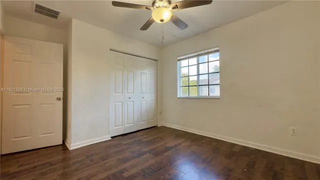 an empty room with wooden floor chandelier fan and windows