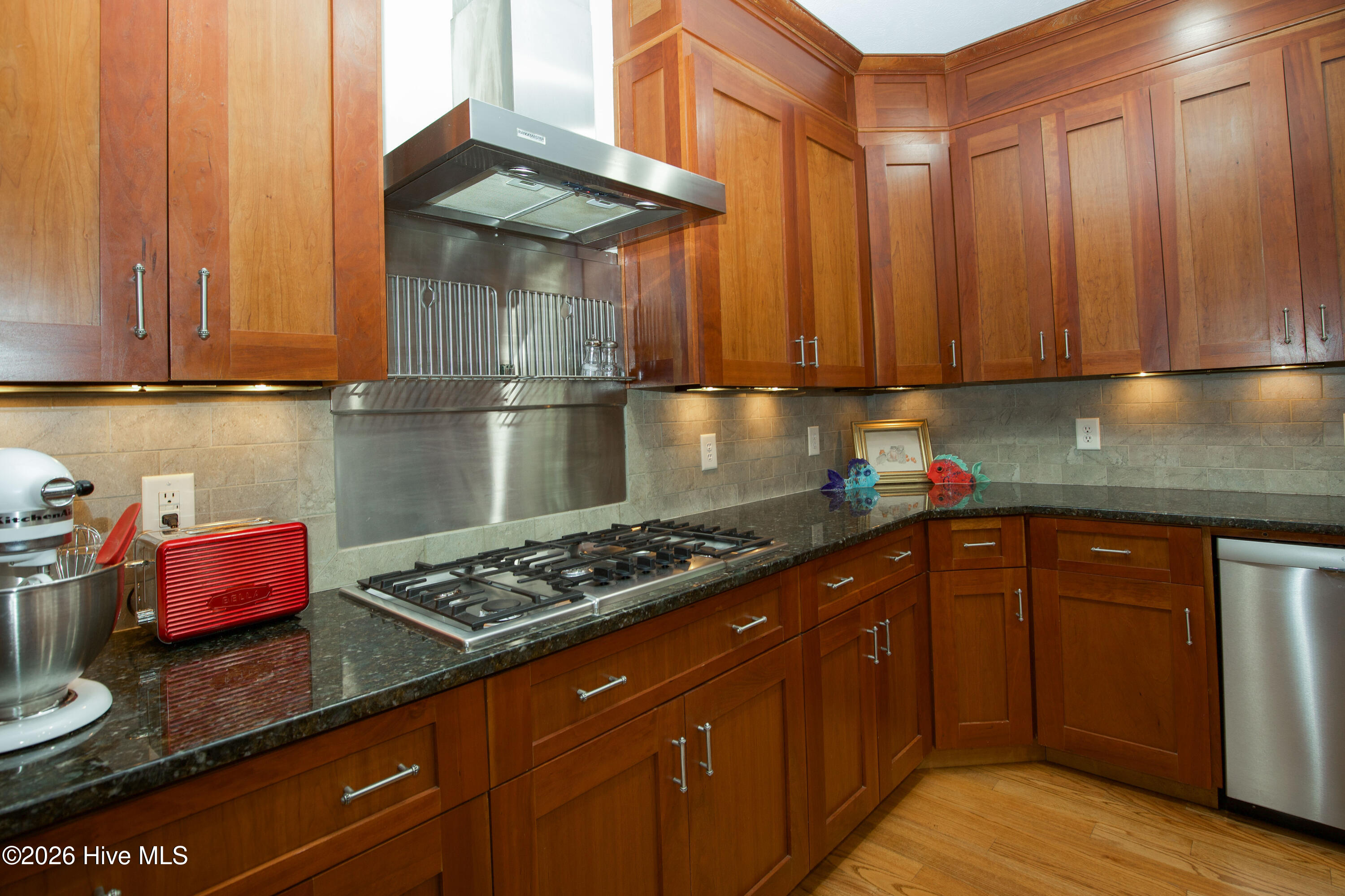 45 Richmond Road Jackson Springs, NC 27281 - Photo 21 of 93 A closer look at the gourmet kitchen at 45 Richmond Rd highlights the sleek stainless steel gas cooktop, striking vent hood, and custom cabinetry with soft-close drawers. Granite countertops and a stylish tile backsplash complete this well-appointed space, perfect for culinary enthusiasts seeking both form and function.