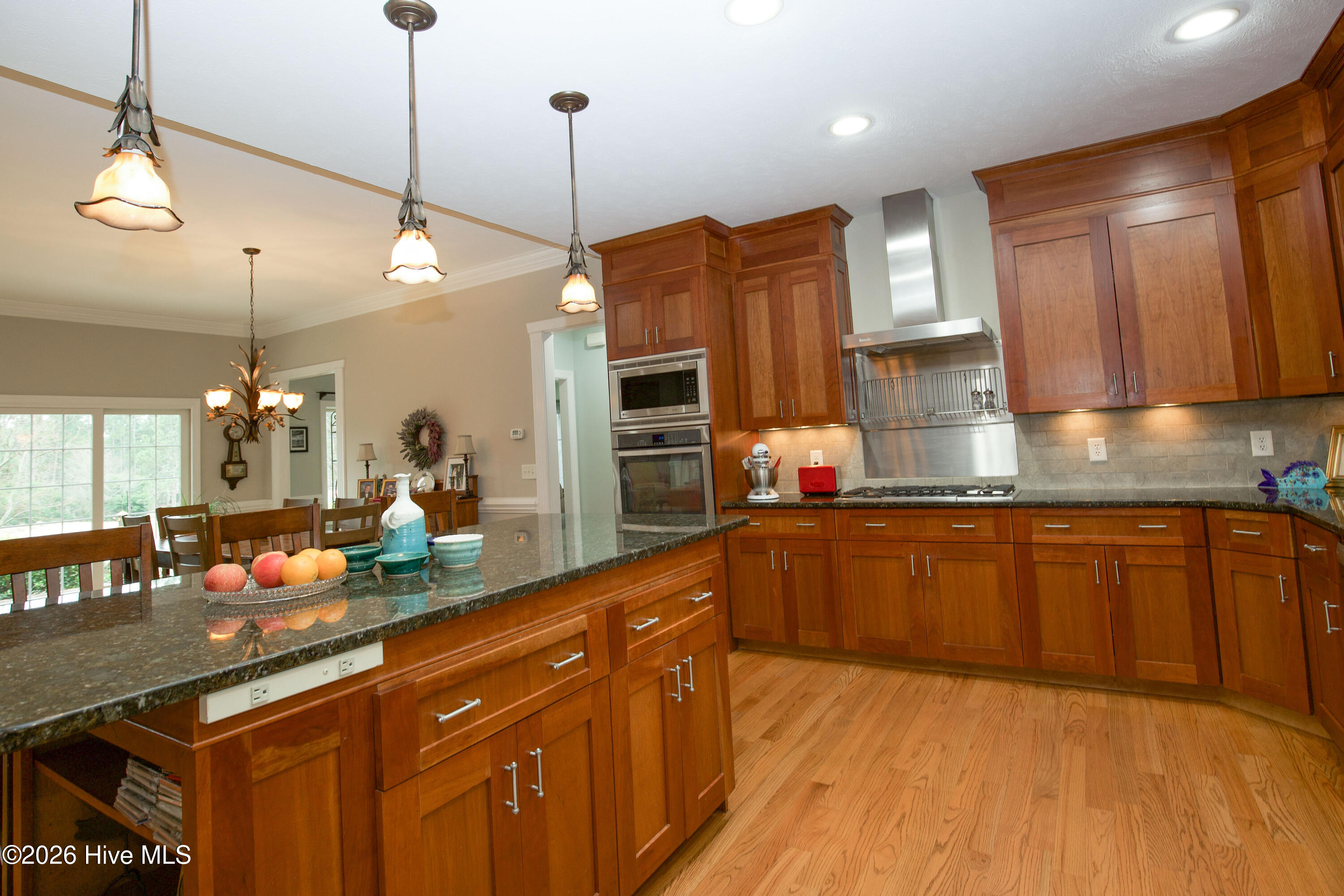 45 Richmond Road Jackson Springs, NC 27281 - Photo 24 of 93 Warm and inviting kitchen at 45 Richmond Rd, featuring rich wood cabinetry, a sleek stainless-steel range hood, and a spacious granite island with ample seating. Perfectly positioned for entertaining, the kitchen opens to the dining area and offers views of the serene backyard through large glass doors.