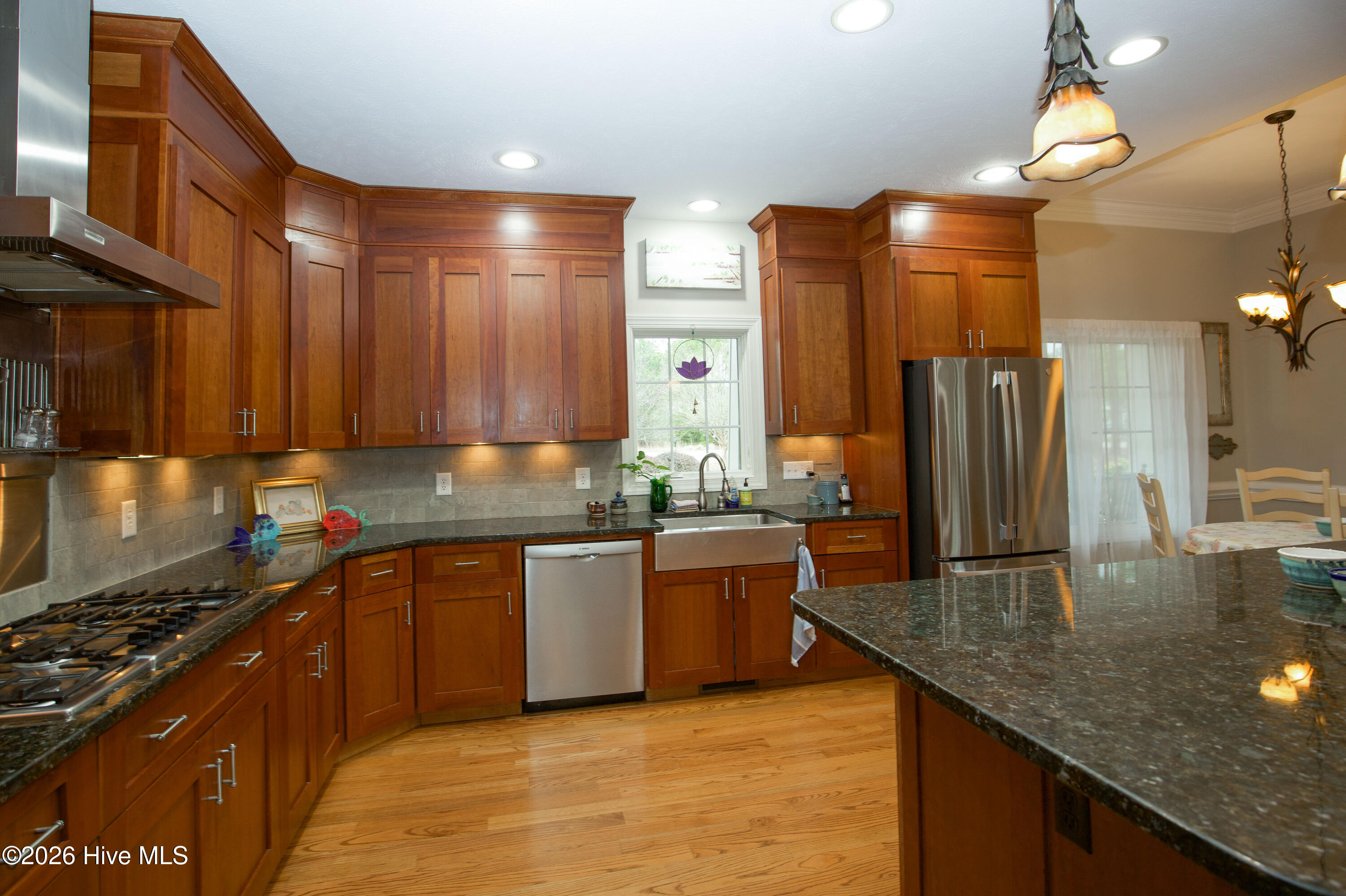 45 Richmond Road Jackson Springs, NC 27281 - Photo 25 of 93 Elegant kitchen at 45 Richmond Rd showcasing rich wood cabinetry, granite countertops, and a farmhouse-style sink under a bright window. The stainless steel appliances and expansive prep space make this a chef’s dream, while natural light and open sightlines to the dining area add to the home's warm, inviting ambiance.