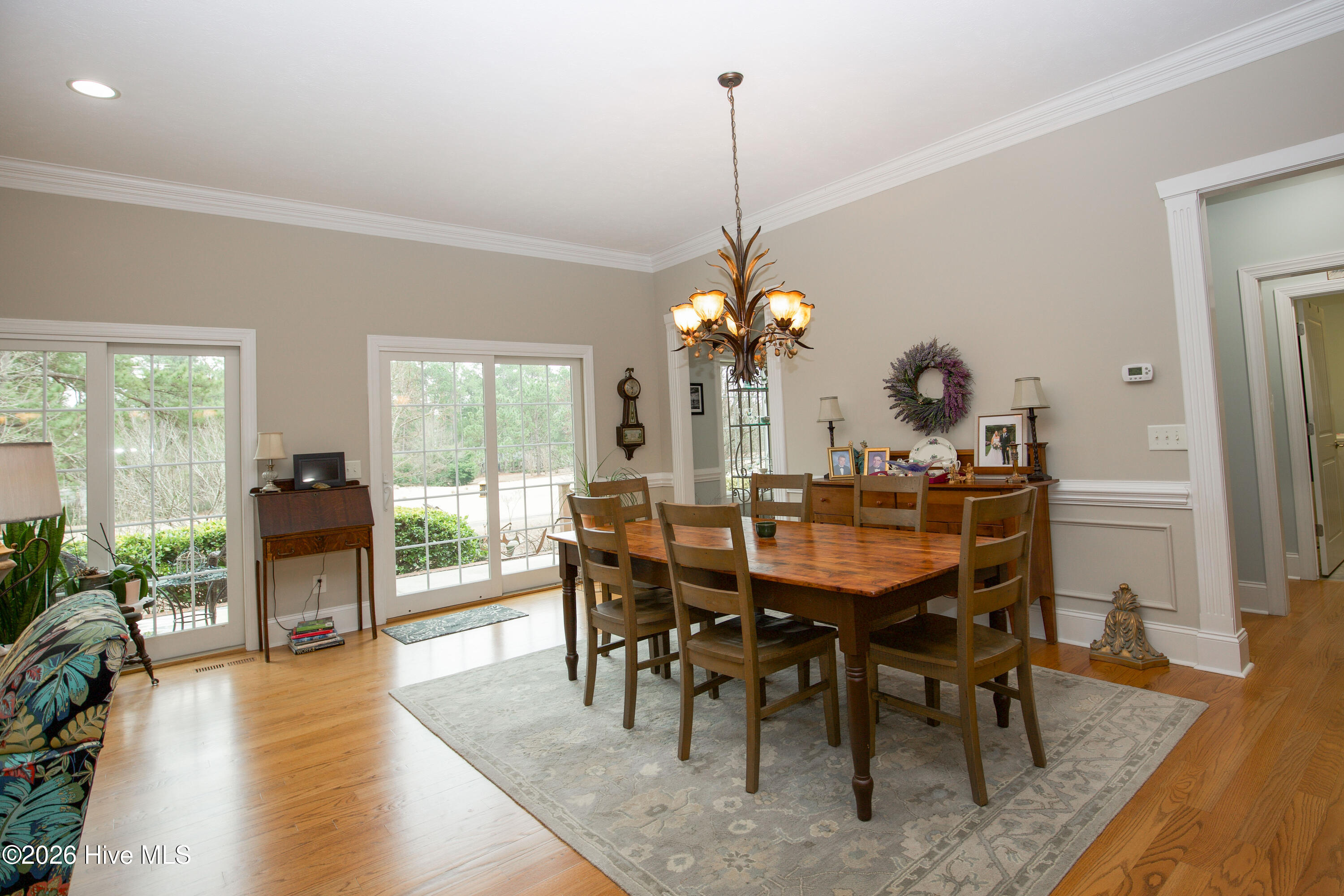 45 Richmond Road Jackson Springs, NC 27281 - Photo 44 of 93 This sun-filled dining space at 45 Richmond Rd in Jackson Springs (Foxfire), NC offers stunning views of the outdoors through expansive sliding glass doors, bringing in natural light and creating a seamless connection to the patio and backyard. Beautiful crown molding, wainscoting, and warm hardwood floors enhance the charm and elegance of this gathering space. Perfect for everyday meals or entertaining, this room is both functional and inviting in the heart of this serene Foxfire home.