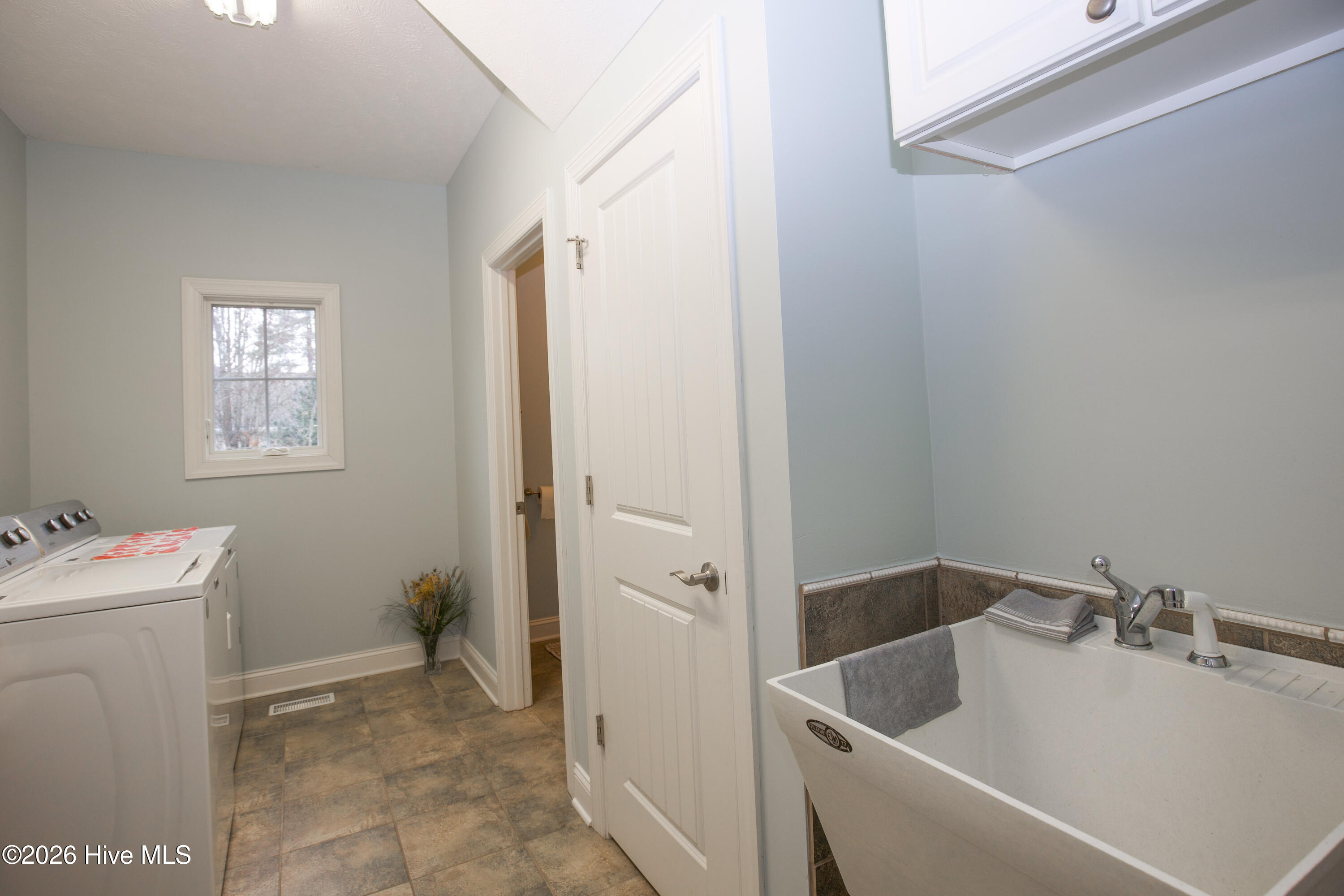 45 Richmond Road Jackson Springs, NC 27281 - Photo 54 of 93 This bright and spacious laundry room is designed for convenience and utility. It features a deep utility sink with a tile backsplash, overhead cabinetry for storage, and a side-by-side washer and dryer setup. A large window brings in natural light, and the durable tile flooring ensures easy maintenance. Whether tackling daily laundry or cleaning up after projects, this space makes household chores feel effortless.