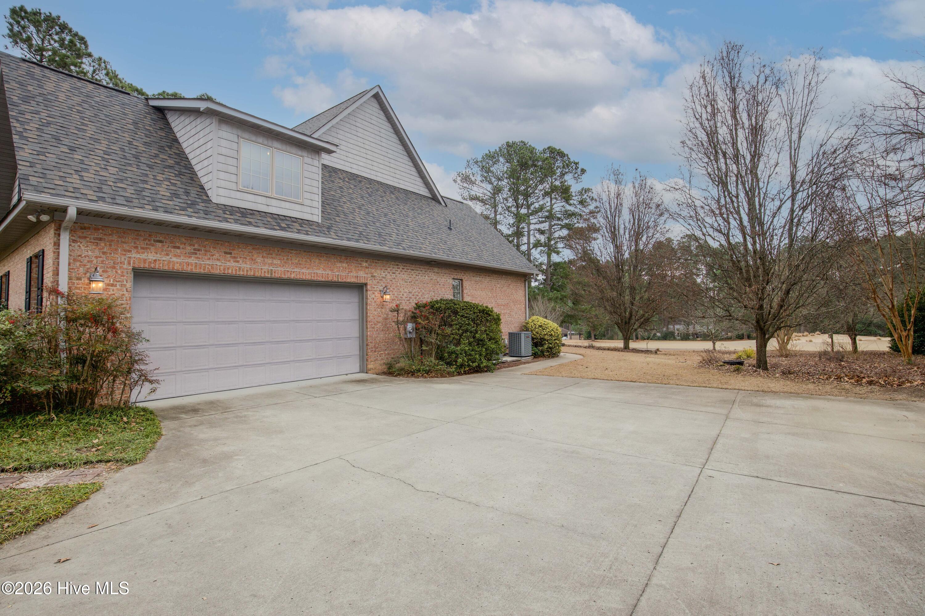 45 Richmond Road Jackson Springs, NC 27281 - Photo 90 of 93 The wide concrete driveway leads to a spacious side-entry garage, offering ample parking for guests and easy access to the home. Surrounded by mature trees and landscaping, and featuring a brand new roof above, this area combines functionality with privacy and golf course views in peaceful Foxfire Village.