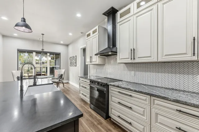 a kitchen with stainless steel appliances granite countertop a stove a sink and white cabinets with wooden floor