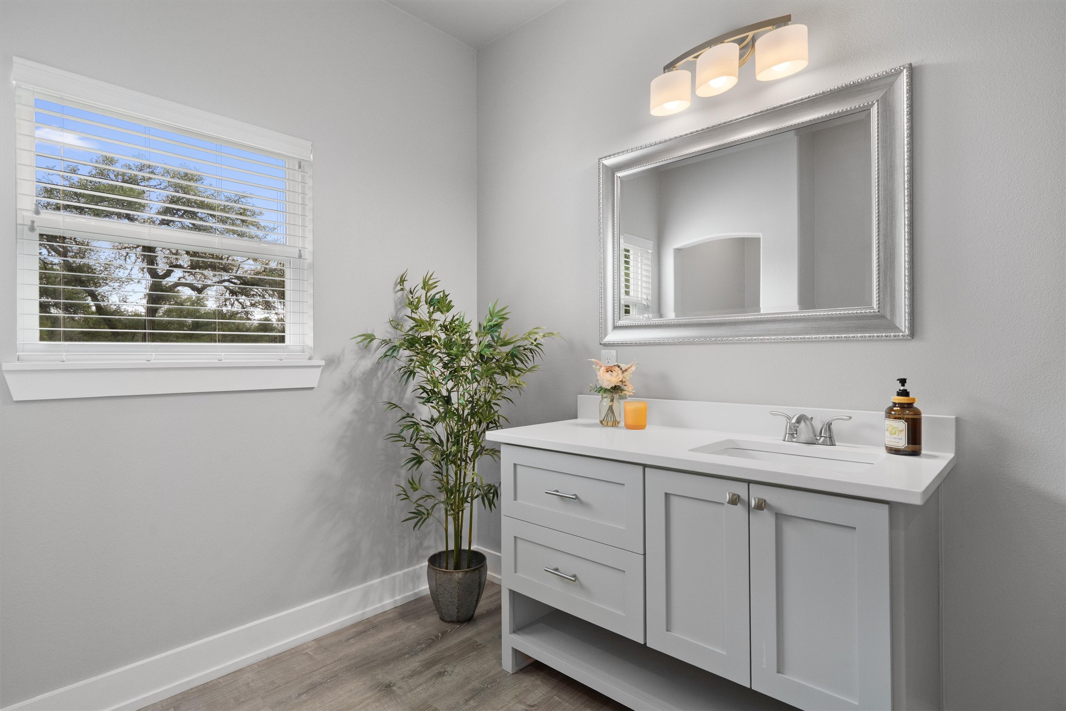 13105 Rooster Springs Road Austin, TX 78737 - Photo 15 of 38 This bathroom features a single vanity with a white countertop and light gray cabinetry, a decorative framed mirror, and a window with blinds