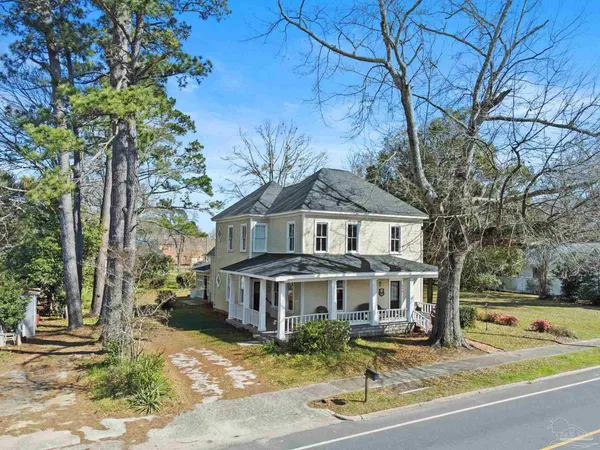 a view of a white house with a large tree and yard