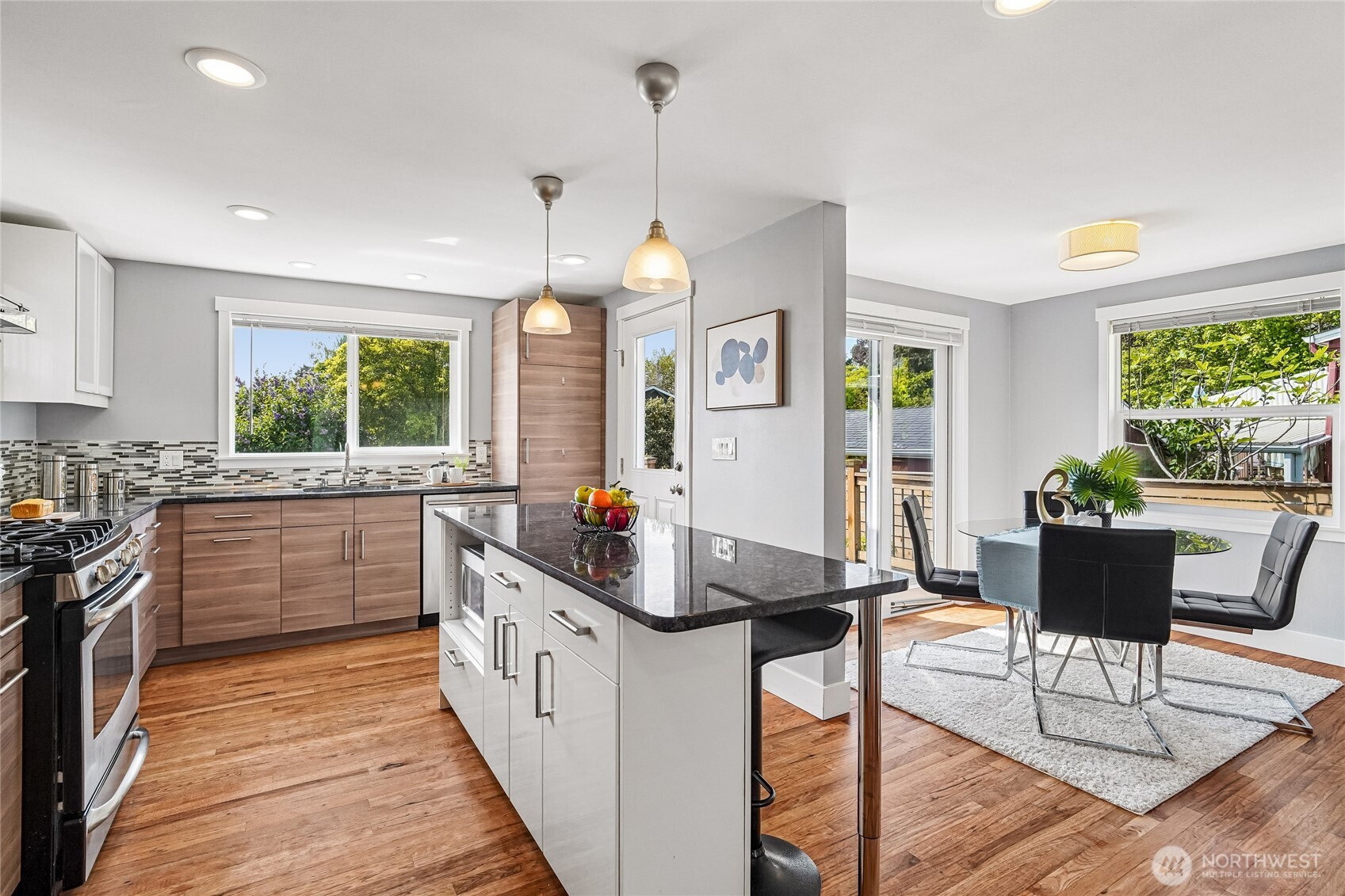7313 25th Avenue Northwest Seattle, WA 98117 - Photo 10 of 40 a kitchen with stainless steel appliances kitchen island granite countertop a stove a sink dishwasher a dining table and chairs with wooden floor