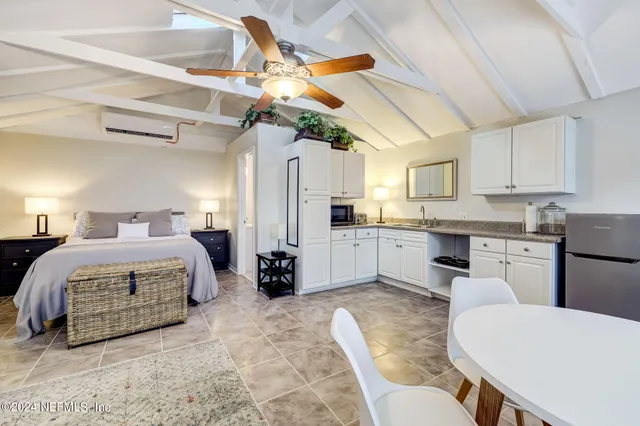 a spacious bedroom with a bed a chandelier with the view of kitchen