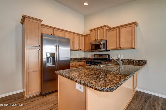 a kitchen with stainless steel appliances granite countertop a refrigerator a stove and a sink with wooden floor