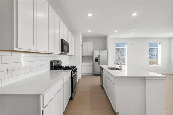a kitchen with stainless steel appliances a sink a stove a refrigerator a white cabinets and a counter top space