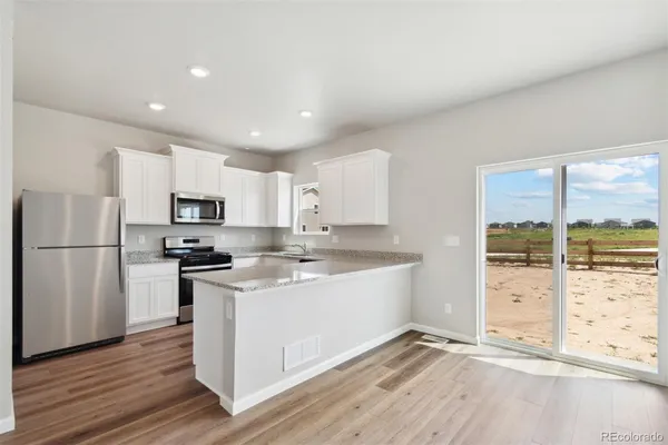 a kitchen with stainless steel appliances a stove a refrigerator a sink and white cabinets with wooden floor next to windows