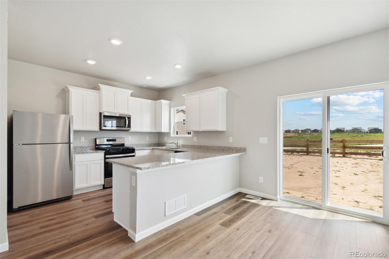 7402 Crystal Avenue Frederick, CO 80530 - Photo 5 of 26 a kitchen with stainless steel appliances a stove a refrigerator a sink and white cabinets with wooden floor next to windows