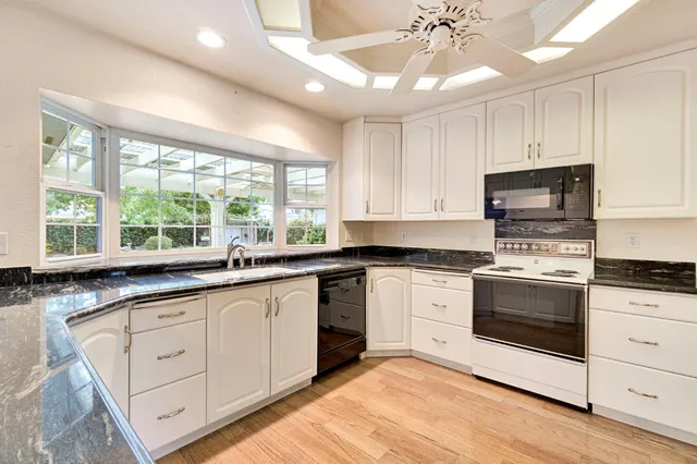 a kitchen with granite countertop white cabinets white stainless steel appliances a sink and a window