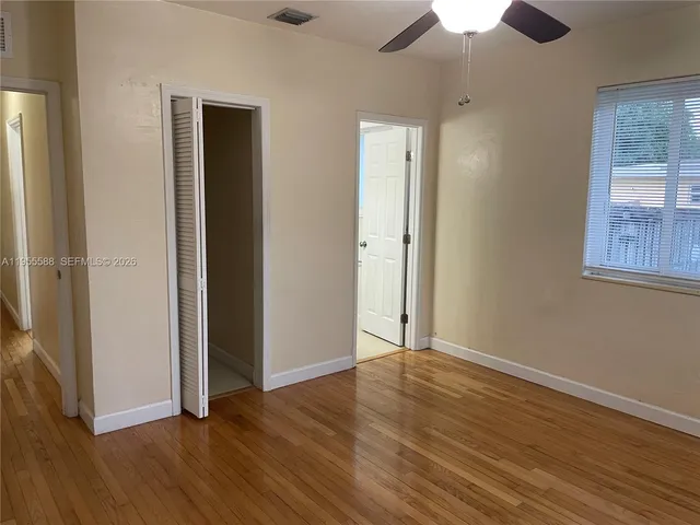an empty room with wooden floor chandelier fan and windows