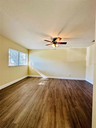 an empty room with wooden floor fan and windows