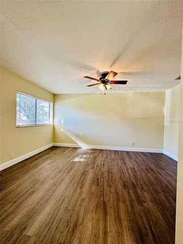an empty room with wooden floor fan and windows