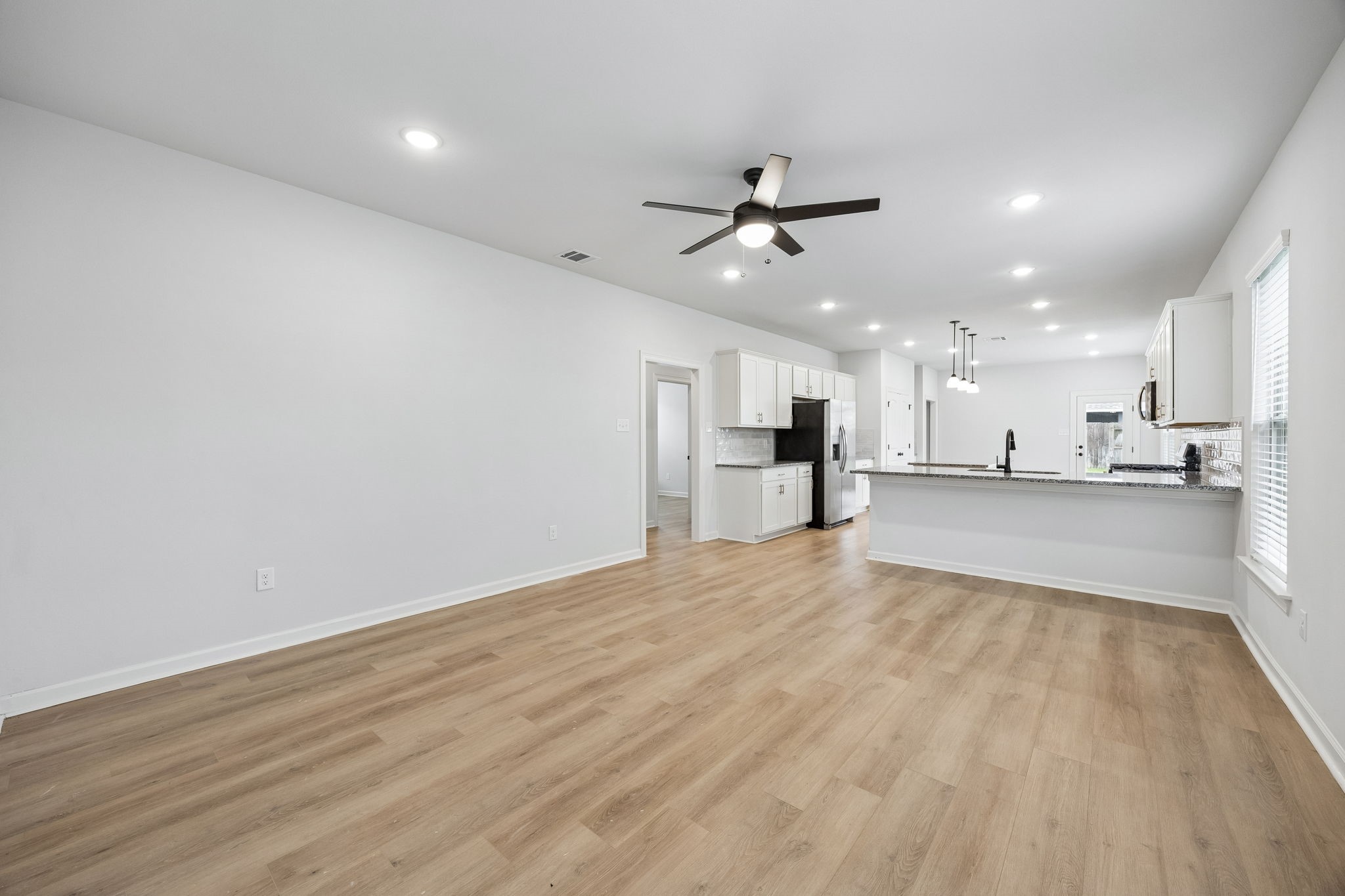 10902 Bonfire Trail Beasley, TX 77417 - Photo 2 of 36 This photo showcases a spacious open-concept living area with light vinyl plank flooring and a modern kitchen featuring white cabinets, stainless steel appliances, and a large island. The room is well-lit with recessed lighting and a ceiling fan, creating a bright and inviting atmosphere.