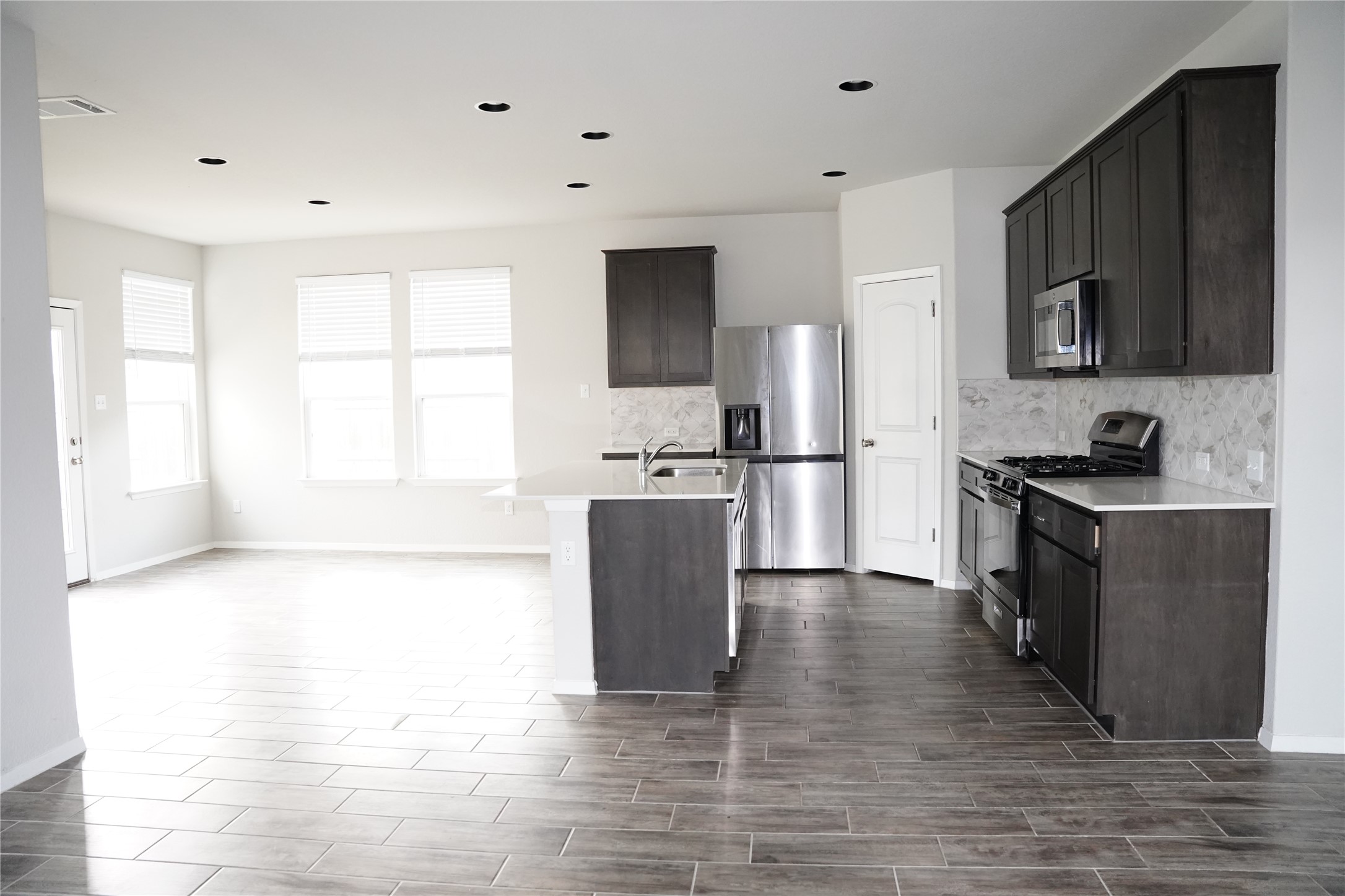 117 Crescent Street Georgetown, TX 78626 - Photo 12 of 38 A well-appointed kitchen and living space, featuring dark cabinetry, stainless steel appliances, and sleek tile flooring.